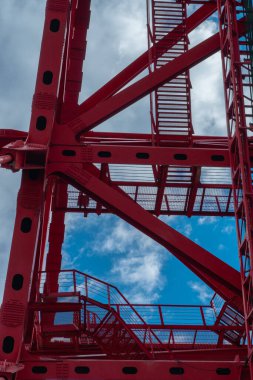 Mavi gökyüzü ve bulutların arka planında kırmızı metal yüksek merdiven yapıları, dikey desen veya doku