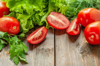 Bahçede yetişen taze kıvırcık salata ve ahşap bir masada sulu olgun domatesler.