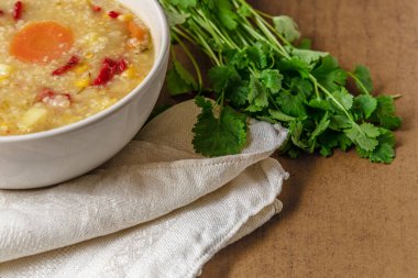 Seramik kasede bulgur ve mısır bulunan sağlıklı vejetaryen sebze çorbası keten peçete ve taze kişniş otu yakın plan.