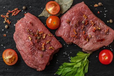 Siyah bir sayfada kiraz domatesli, baharatlı ve otlu taze çiğ et.