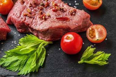 Siyah bir sayfada kiraz domatesli, baharatlı ve otlu taze çiğ et.