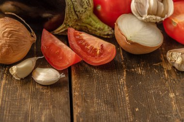 Patlıcan sote için sebzeler: patlıcan, domates, soğan ve ahşap bir masada sarımsak.