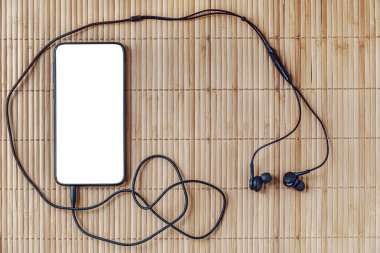 Bej bambu yüzeyinde kulaklıklı akıllı telefon, üst görünüm, taklit et.