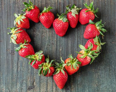 Kokulu olgun çilekler kalp şeklinde eski ahşap bir masanın üzerine serilmiş, düz bir şekilde.