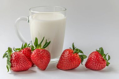 Beyaz bir yüzey üzerinde cam bardak süt ve tatlı kokulu çilekler.