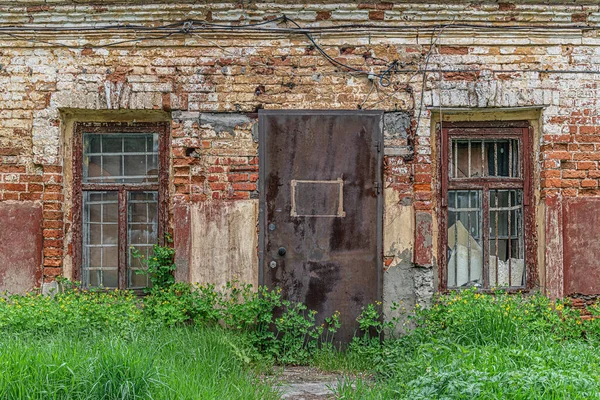 shabby brick wall, windows and locked door of abandoned old factory