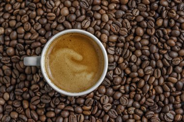 Kahve çekirdekleri arasında beyaz bir porselen fincanda taze demlenmiş aromatik kahve.