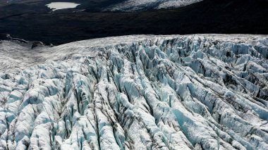 İzlanda 'daki Fjallsjokull buzulunu çevreleyen karanlık volkanik dağların hava manzarası. İzlanda 'daki Fjalsjokull buzulunun donmuş yüzeyinin hava görüntüsü..