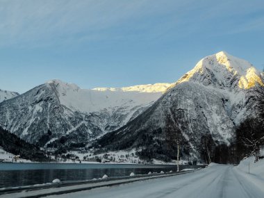 Gün doğumunda Norveç 'teki dağların ve ormanların içinden arabayla geçmek. Bir dağın tepesinde gün ışığı.