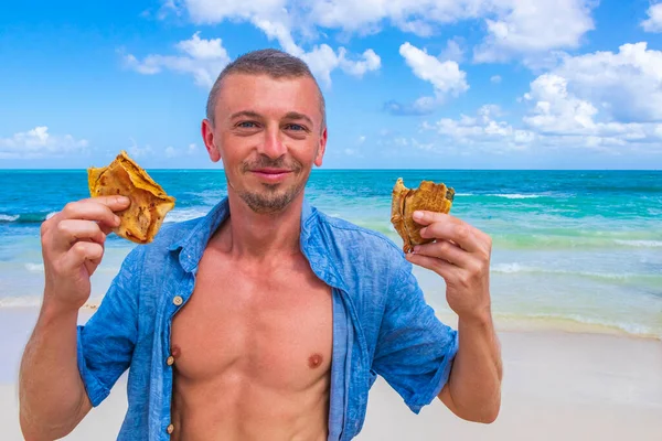 Russian male tourist is trying mexican food empanadas at the beach in Playa del Carmen Mexico.