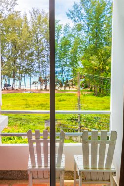 Nai Thon Naithon Sahili Sakhu Thalang Phuket Tayland 'daki beyaz balkon sandalyelerinden ağaçların arkasındaki rüya körfezi manzarası.