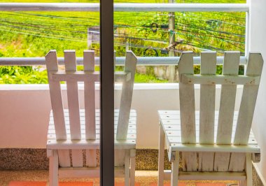 Nai Thon Naithon Sahili Sakhu Thalang Phuket Tayland 'daki beyaz balkon sandalyelerinden ağaçların arkasındaki rüya körfezi manzarası.