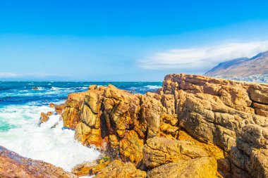 Glencairn Simons Kasabası Cape Town Batı Afrika Burnu 'nda kaya dalgaları ve bulutlu dağlarla sahte körfez manzarası.