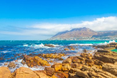 Glencairn Simons Kasabası Cape Town Batı Afrika Burnu 'nda kaya dalgaları ve bulutlu dağlarla sahte körfez manzarası.