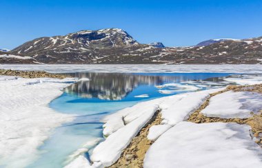 Yaz manzarasında donmuş turkuaz göl Vavatn manzarası ve Hemsedal Norveç 'te karlı dağlar.