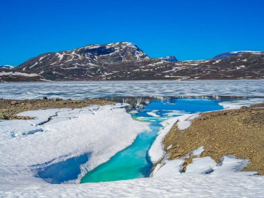 Yaz manzarasında donmuş turkuaz göl Vavatn manzarası ve Hemsedal Norveç 'te karlı dağlar.