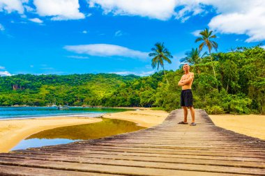 Mangrove sahilindeki ahşap köprüde turist gezgini ve büyük tropik ada Ilha Grande Rio de Janeiro Brezilya 'daki Pouso plajı..