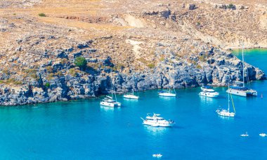 Lindos Sahili panorama manzarası turkuaz berrak su botu turistleri ve Rodos Yunanistan 'da güneş görüyor.