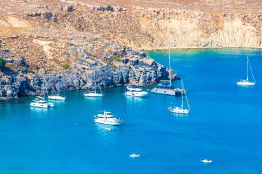 Lindos Sahili panorama manzarası turkuaz berrak su botu turistleri ve Rodos Yunanistan 'da güneş görüyor.