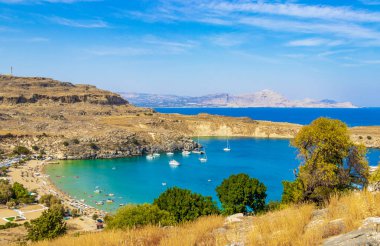 Lindos Sahili panorama manzarası turkuaz berrak su botu turistleri ve Rodos Yunanistan 'da güneş görüyor.