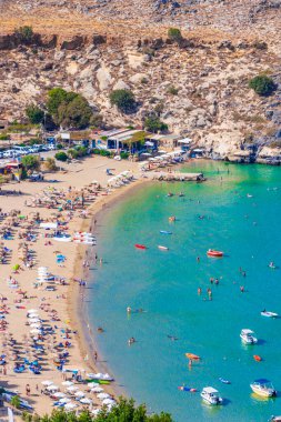 Lindos Sahili panorama manzarası turkuaz berrak su botu turistleri ve Rodos Yunanistan 'da güneş görüyor.