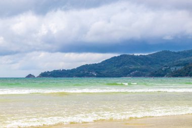 Patong Beach bay sea coast panorama view with turquoise blue clear water waves white sand and green mountains and palm trees in Patong Beach Kathu District Phuket Island Province Southern Thailand.