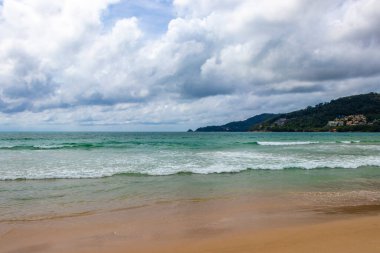 Patong Beach bay sea coast panorama view with turquoise blue clear water waves white sand and green mountains and palm trees in Patong Beach Kathu District Phuket Island Province Southern Thailand.