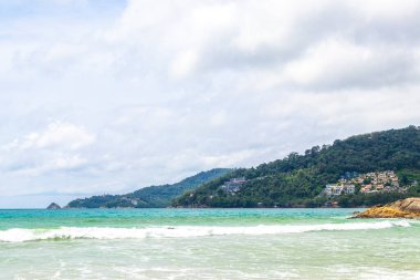 Patong Beach bay sea coast panorama view with turquoise blue clear water waves white sand and green mountains and palm trees in Patong Beach Kathu District Phuket Island Province Southern Thailand.
