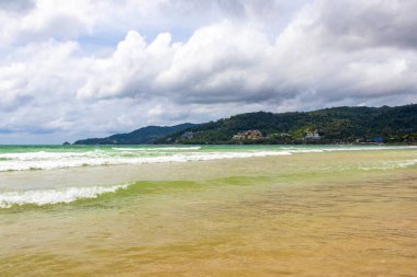 Patong Beach bay sea coast panorama view with turquoise blue clear water waves white sand and green mountains and palm trees in Patong Beach Kathu District Phuket Island Province Southern Thailand.