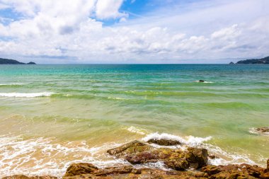 Patong Beach bay sea coast panorama view with turquoise blue clear water waves white sand and green mountains and palm trees in Patong Beach Kathu District Phuket Island Province Southern Thailand.