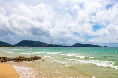 Patong Beach bay sea coast panorama view with turquoise blue clear water waves white sand and green mountains and palm trees in Patong Beach Kathu District Phuket Island Province Southern Thailand.