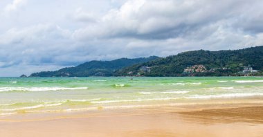 Patong Beach bay sea coast panorama view with turquoise blue clear water waves white sand and green mountains and palm trees in Patong Beach Kathu District Phuket Island Province Southern Thailand.