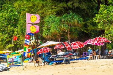 Kathu Phuket Tayland 08. Ekim 2025 Patong Sahili manzaralı gezinti turistleri mavi su dalgaları güneş şemsiyeleri cankurtaran kuleleri dağlar ve Tayland palmiyeleri.