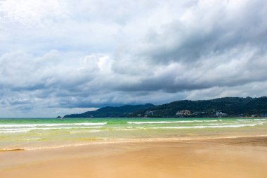 Patong Beach bay sea coast panorama view with turquoise blue clear water waves white sand and green mountains and palm trees in Patong Beach Kathu District Phuket Island Province Southern Thailand.