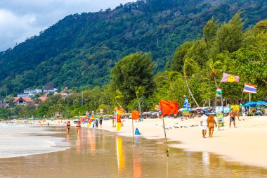 Kathu Phuket Tayland 08. Ekim 2025 Patong Sahili manzaralı gezinti turistleri mavi su dalgaları güneş şemsiyeleri cankurtaran kuleleri dağlar ve Tayland palmiyeleri.