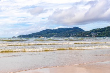 Patong Beach bay sea coast panorama view with turquoise blue clear water waves white sand and green mountains and palm trees in Patong Beach Kathu District Phuket Island Province Southern Thailand.