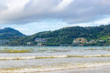 Patong Beach bay sea coast panorama view with turquoise blue clear water waves white sand and green mountains and palm trees in Patong Beach Kathu District Phuket Island Province Southern Thailand.