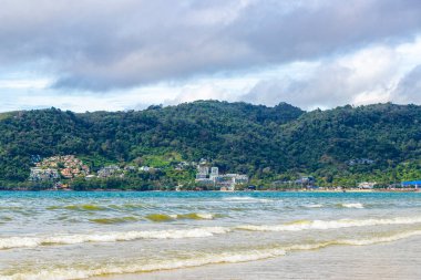 Patong Beach bay sea coast panorama view with turquoise blue clear water waves white sand and green mountains and palm trees in Patong Beach Kathu District Phuket Island Province Southern Thailand.
