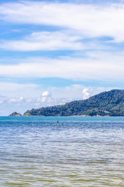 Patong Beach bay sea coast panorama view with turquoise blue clear water waves white sand and green mountains and palm trees in Patong Beach Kathu District Phuket Island Province Southern Thailand.