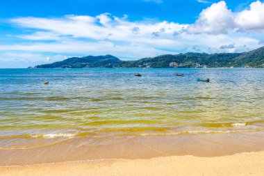 Patong Beach bay sea coast panorama view with turquoise blue clear water waves white sand and green mountains and palm trees in Patong Beach Kathu District Phuket Island Province Southern Thailand.