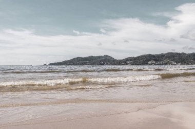 Patong Beach bay sea coast panorama view with turquoise blue clear water waves white sand and green mountains and palm trees in Patong Beach Kathu District Phuket Island Province Southern Thailand.
