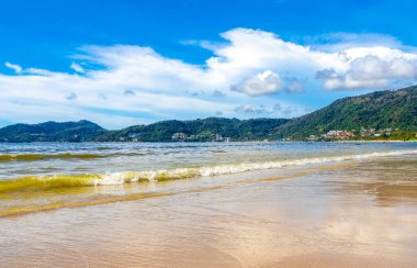 Patong Beach bay sea coast panorama view with turquoise blue clear water waves white sand and green mountains and palm trees in Patong Beach Kathu District Phuket Island Province Southern Thailand.