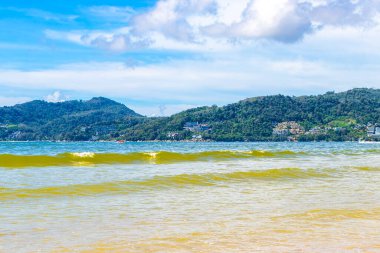 Patong Beach bay sea coast panorama view with turquoise blue clear water waves white sand and green mountains and palm trees in Patong Beach Kathu District Phuket Island Province Southern Thailand.