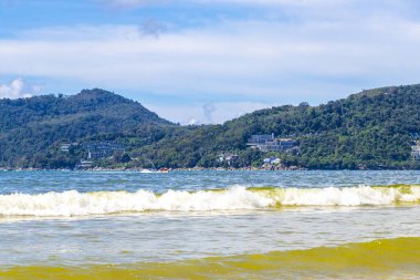 Patong Beach bay sea coast panorama view with turquoise blue clear water waves white sand and green mountains and palm trees in Patong Beach Kathu District Phuket Island Province Southern Thailand.