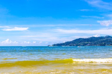 Patong Beach bay sea coast panorama view with turquoise blue clear water waves white sand and green mountains and palm trees in Patong Beach Kathu District Phuket Island Province Southern Thailand.