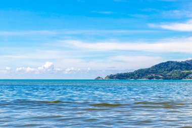 Patong Beach bay sea coast panorama view with turquoise blue clear water waves white sand and green mountains and palm trees in Patong Beach Kathu District Phuket Island Province Southern Thailand.