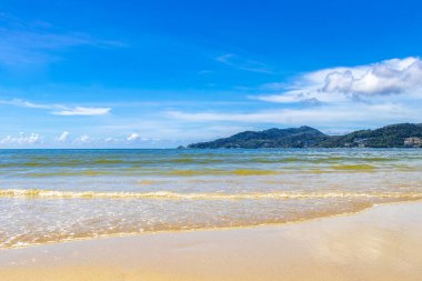 Patong Beach bay sea coast panorama view with turquoise blue clear water waves white sand and green mountains and palm trees in Patong Beach Kathu District Phuket Island Province Southern Thailand.