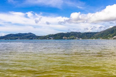 Patong Beach bay sea coast panorama view with turquoise blue clear water waves white sand and green mountains and palm trees in Patong Beach Kathu District Phuket Island Province Southern Thailand.