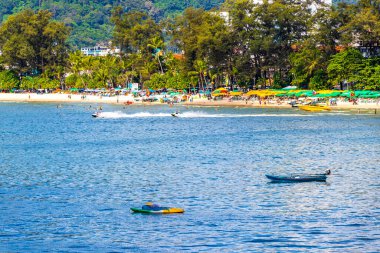 Kathu Phuket Tayland 13 numara. Ekim 2025 Patong Sahili manzaralı gezinti turistleri mavi su dalgaları güneş şemsiyeleri cankurtaran kuleleri dağlar ve Tayland palmiyeleri.