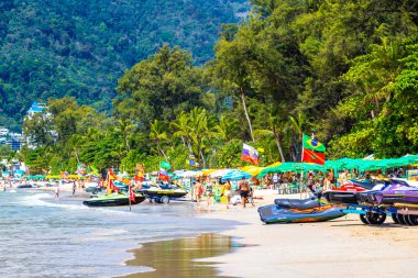Kathu Phuket Tayland 13 numara. Ekim 2025 Patong Sahili manzaralı gezinti turistleri mavi su dalgaları güneş şemsiyeleri cankurtaran kuleleri dağlar ve Tayland palmiyeleri.